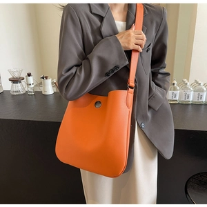 Detail of orange lychee leather shoulder bag with circular metal horse head buckle