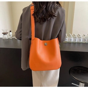 Close-up of bright orange litchi grain PU leather crossbody bag with wide strap detail