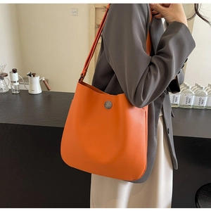 Detail of orange pebble leather bucket bag with silver metal emblem on a model