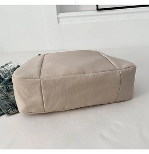 Detail view of the wide bottom design on a beige canvas dumpling crossbody bag