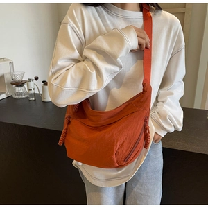 Detail view of the orange crescent crossbody bag with woven zipper pulls and wide strap
