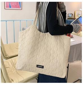 Detail of beige tote bag featuring heart quilted texture and black woven label on shoulder