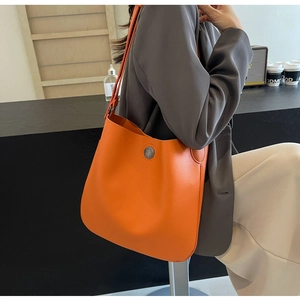 Detail of a bright orange PU leather tote bag with a vintage metal buckle on a model