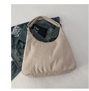 Flat lay of a beige nylon crescent bag with wide shoulder strap on white fabric