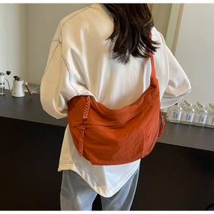 Detail of a large orange crescent messenger bag featuring a braided rope zipper pull