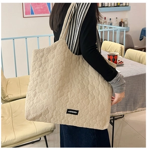Detailed view of the beige tote bag featuring heart quilted texture and brand label