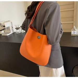 Detail of orange faux leather tote bag with vintage horse badge and wide shoulder strap