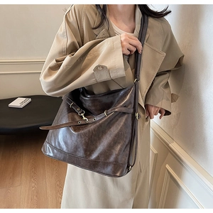 Detail of a large dark brown leather tote bag with gold hardware on a khaki coat
