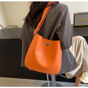 Close-up of bright orange lychee grain leather shoulder bag with round metal buckle