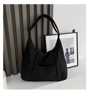 Detail of black quilted nylon dumpling bag with wide shoulder strap in minimalist setting