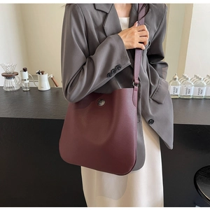 Detail view of burgundy leather tote bag with round metal buckle and wide shoulder strap