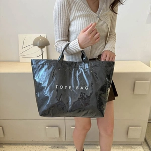 Close-up of black glossy patent leather tote bag with white TOTE BAG text print