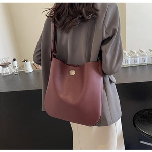 Close-up of a burgundy lychee grain leather tote bag with a round vintage metal buckle