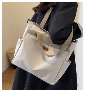 Detail of off-white canvas tote bag featuring khaki handles and leather logo patch