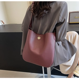 Detail view of burgundy pebble leather shoulder bag with silver circular metal emblem