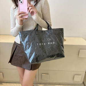 Glossy black waterproof tote bag with white TOTE BAG text print in a lifestyle setting