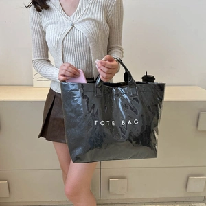 Close-up of black glossy DuPont paper tote bag with bold TOTE BAG lettering and spacious interior