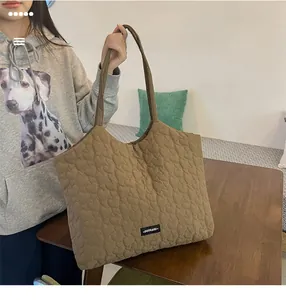 Close-up of brown quilted tote bag featuring heart pattern stitching and brand logo label