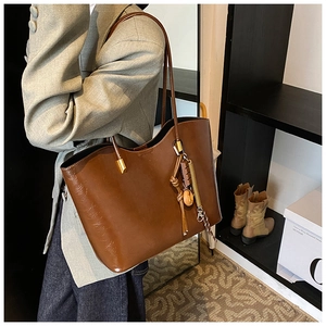 Détail d'un grand sac cabas en similicuir marron foncé avec bandoulière et pendentif chic