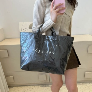 Model showing a large black glossy tote bag with white TOTE BAG lettering detail