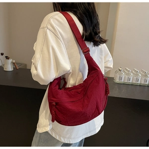 Detail of burgundy crescent dumpling bag with textured fabric and woven zipper pull