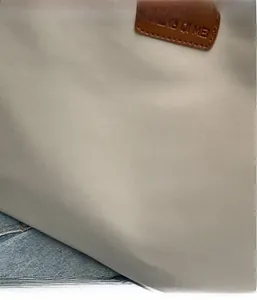 Detailed close-up of a canvas tote bag with a brown leather logo patch and fine texture
