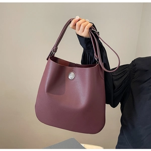 Detail of burgundy PU leather bucket bag with silver emblem and wide shoulder strap