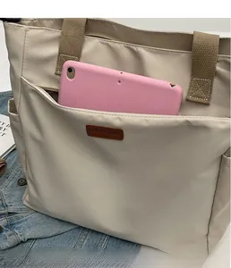 Detail of beige canvas tote bag with front zipper pocket and leather logo patch
