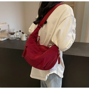 Detail view of a dark red nylon dumpling bag with adjustable strap in a cafe setting