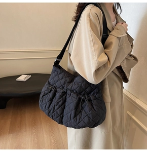 Close-up of black quilted nylon tote bag with drawstring side pockets on beige trench coat