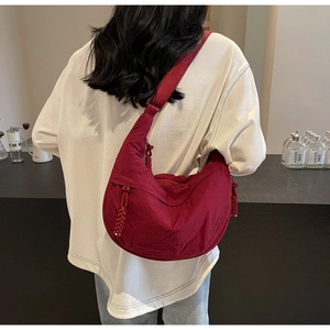 Detail of burgundy crescent dumpling bag with woven zipper pull and adjustable strap