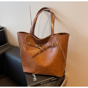 Brown PU leather tote bag with long handles and gold metal buckles on a black bench