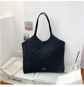 Detail of black tote bag featuring heart-shaped quilted texture and small logo tag