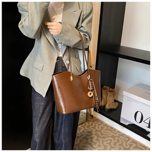 Détail d'un grand sac cabas marron foncé en cuir brillant avec pendentif métallique élégant