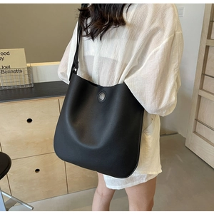 Detail of black pebbled leather bucket bag with horse-carriage metal emblem on front