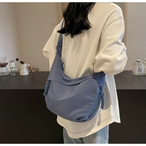 Detail of blue crescent crossbody bag featuring adjustable strap and woven zipper pull