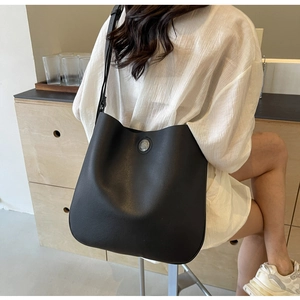 Detail of black pebble-textured PU leather tote bag with a silver round metal buckle
