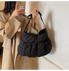 Detail of black quilted nylon shoulder bag showing rhombus pattern and drawstring side pocket