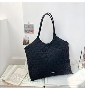 Detailed macro view of black quilted heart patterns on a soft fabric shoulder bag