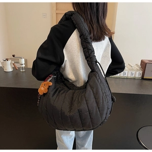 Close-up of black quilted cloud bag with plush bear charm on a minimalist wide strap