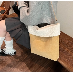 Detail showing plush faux shearling trim on yellow suede bucket bag during model carry