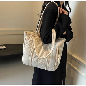 Close-up of beige quilted tote bag texture with shoulder straps on model outfit