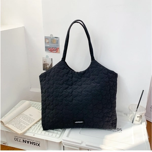 Minimalist black quilted tote bag with embossed heart pattern and wide shoulder straps