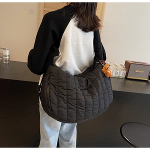 Detail of a black quilted crescent shoulder bag with a cute brown bear charm on the side
