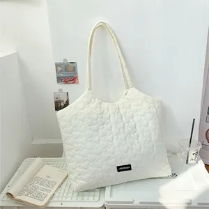Minimalist white heart-quilted shoulder bag with stylish woven label in an indoor setting