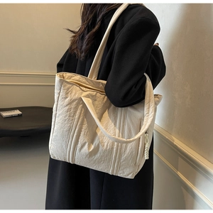 Detail of a large off-white pleated tote bag showing fabric texture and double straps