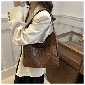 Detail of a brown woven PU leather tote bag in crescent shape worn by a model