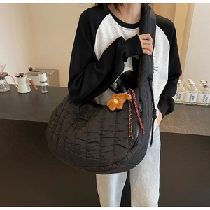 Detail of black quilted shoulder bag with plush bear charm worn by a model