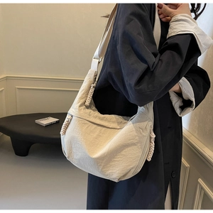 Detail of beige crescent dumpling bag showing waterproof nylon fabric and woven rope zipper