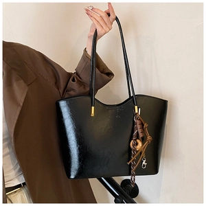 Détail d'un grand sac cabas noir brillant avec boucles dorées et breloques de mode